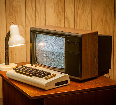 Product photo of an old commodore vic-20 vintage retro computer on wood desk, an 80's lamp and wood panelling in the back.